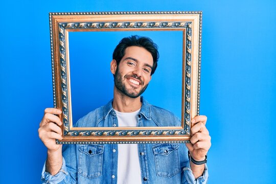 Young hispanic man holding empty frame smiling with a happy and cool smile on face. showing teeth.