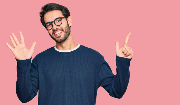 Young hispanic man wearing casual clothes and glasses showing and pointing up with fingers number seven while smiling confident and happy.