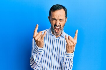 Naklejka premium Middle age hispanic man wearing casual clothes shouting with crazy expression doing rock symbol with hands up. music star. heavy concept.