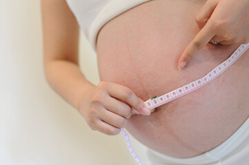 Pregnant Asian woman measuring her belly at home