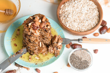 homemade oatmeal banana pancakes with chia seeds, almonds, prunes and dates, drizzled with honey and crushed nuts on a dark background. diet breakfast is healthy for the figure . close-up