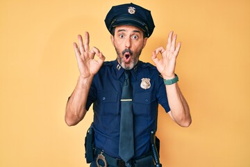 Middle age hispanic man wearing police uniform looking surprised and shocked doing ok approval symbol with fingers. crazy expression