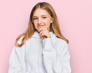 Beautiful young caucasian girl wearing casual sweatshirt looking confident at the camera with smile with crossed arms and hand raised on chin. thinking positive.