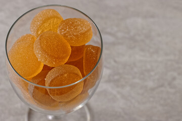 Orange round sugar coated jelly candies in glass on gray background with copy space.
