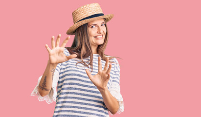 Beautiful caucasian woman wearing summer hat disgusted expression, displeased and fearful doing disgust face because aversion reaction. with hands raised