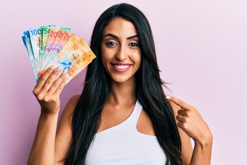 Beautiful hispanic woman holding swiss franc banknotes smiling happy pointing with hand and finger