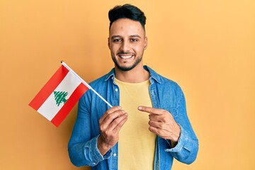 Young arab man holding lebanon flag smiling happy pointing with hand and finger
