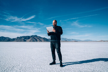 Male explorer browsing tablet in salt pan of Utah state in USA