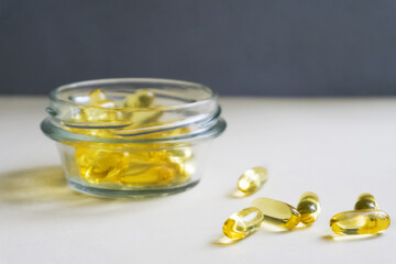 Yellow capsules are scattered on a light background. In the background is a glass jar. Soft focus in the foreground.