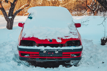 An old red car with no headlights in the snow