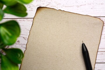 Burnt edge brown paper with space for text with blurred green plant on wooden desk. For text use