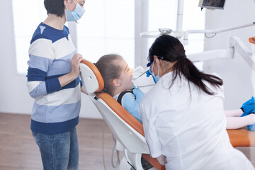 Teeth doctor wearing face mask examining oral hygine of little girl . Dentistry specialist during child cavity consultation in stomatology office using modern technology.