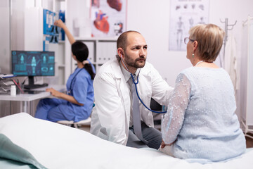 Obraz premium Healthcare specialist using stethoscope in private clinic using stethoscope. Medical practitioner examining lungs of caucasian in modern clinic dressed in white coat.