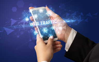 Female hand holding smartphone with WEB TRAFFIC inscription, modern technology concept