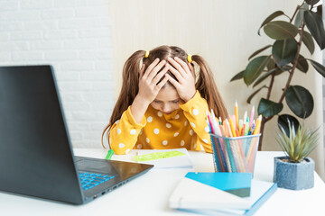 Little girl schoolgirl independently studies new material. Distance learning. Fatigue among schoolchildren. Headache