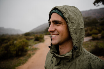 Smiling handsome young male athlete happy with views on mountain path wearing rain jacket for projection from weather