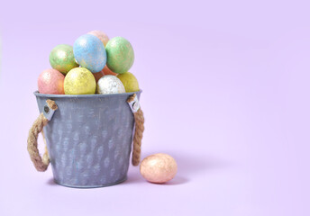 Colorful Easter eggs on a soft purple background in a gray bucket in the style of minimalism. with place for text. Easter background. High quality photo.