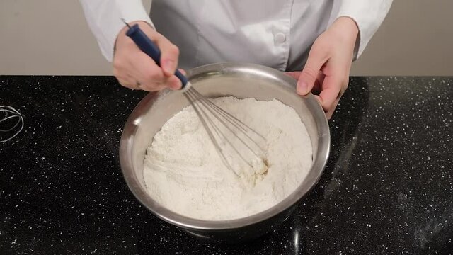 Close up of a woman hands that whisk almond flour in the bowl, preparing dough for macarons.