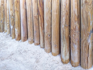 Perspective view of round wooden posts on white sand. Close up of fence made of bamboo poles in the French West Indies. Construction and Architecture concept.