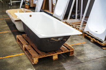 Cast iron bathtub on a wooden pallet. Warehousing and sale of plumbing fixtures in the store. Close-up