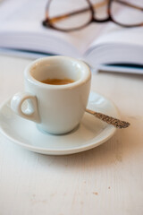 Cup of coffee espresso and book with reading glasses in background