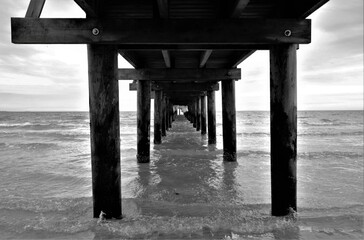 Black and white picture taken under a pier on the beach