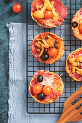 Mini pizza. Small homemade pizza with mushrooms, salami, tomatoes, and cheese on a baking rack.