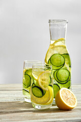 Sassi water with lemon and cucumber in a bottle and glasses on a light wooden background in a high key