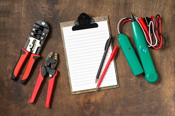 Tools of an electrician-installer or builder on a brown wooden table. Construction tools: crimping, cable tracker, notepad and pens on the table. Top view with copyspace