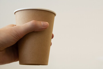 Disposable paper cup close-up in a man's hand. Copy space. Light background