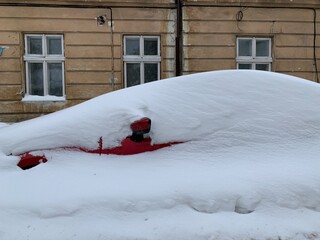 The car was covered with snow in the parking lot. Cars under a large layer of snow. Snowfall on the streets of Europe.