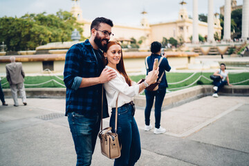 Happy influence bloggers smiling while shooting video vlog about touristic lifestyle, Caucasian male and female millennials enjoying getaway journey for creating selfie content via cellular technology