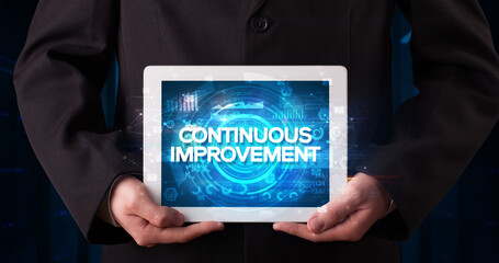 Young business person working on tablet and shows the inscription: CONTINUOUS IMPROVEMENT, business concept
