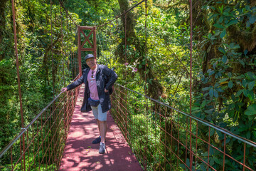 Obraz premium Man - tourist standing in a red suspension bridges in Santa Elena Cloud Forest Reserve, in Monteverde, Costa Rica. Foggy rainforest in the mountains. Central America.