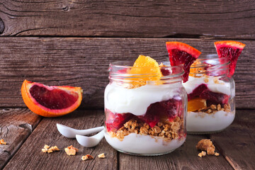 Healthy red blood orange parfaits in mason jars. Scene on dark wood background.