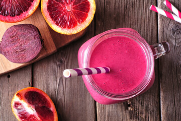 Smoothie with red oranges and beets in a mason jar glass. Close up top view table scene on a rustic wood background.