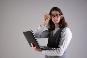 Programming and writing code, developing software products. Geek guy, with long hair and glasses, holding a laptop, gray background