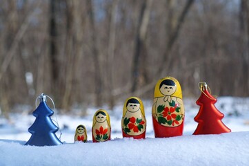 A row of nesting dolls and toy Christmas trees in the winter forest.