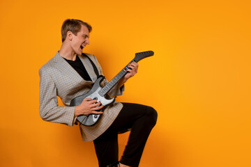 stylish and cool guy in a suit and with a game guitar on a yellow background, have fun and have a good time