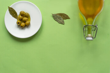 green olives on the plate and olive oil bottle on light green background, top view. Food background