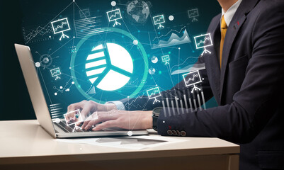 Business hand working on laptop with pie chart icons coming out from the screen, successful business concept