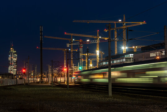 Langzeitbelichtung Zug verl&auml;sst die Station in der Nacht. Im Hintergrund Kr&auml;ne einer Baustelle und ein Wolkenkratzer. Zugsignale in rot und gr&uuml;n.  