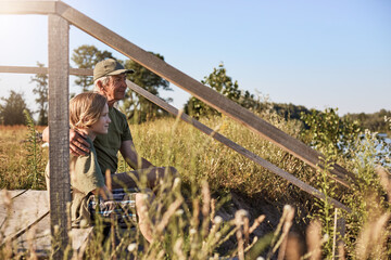 Side view of father and son sitting together looking at green field, enjoying spending time...