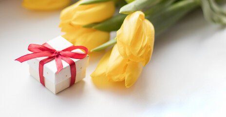 sunlight on yellow tulips near gift box on white, mothers day concept