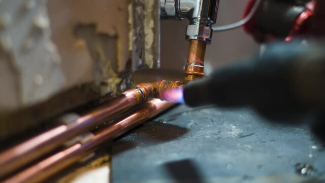 plumber plumbing in new radiator piping with gas torch and solder. home project.