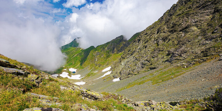 summer landscape of romanian carpathian mountains. wonderful nature scenery with clouds on the peaks and snow in the valley. hills in grass and rocks. travel to fagaras ridge