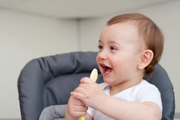 Mother feeding hungry baby in the highchair indoors