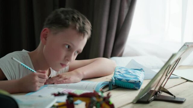 a capable student of 8 years old, writes in a notebook at the table.  the boy is doing his homework. Home schooling.
