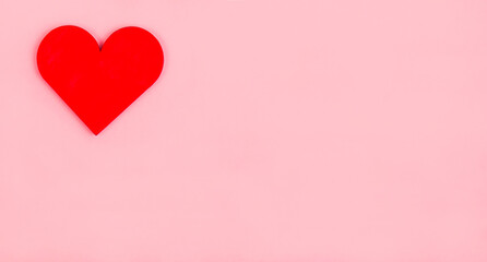 A wooden red heart lies on a pink background. Valentine's Day greeting card.