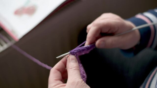 close up of woman knitting with purple whool at home to create a doll. focus on knitting needle